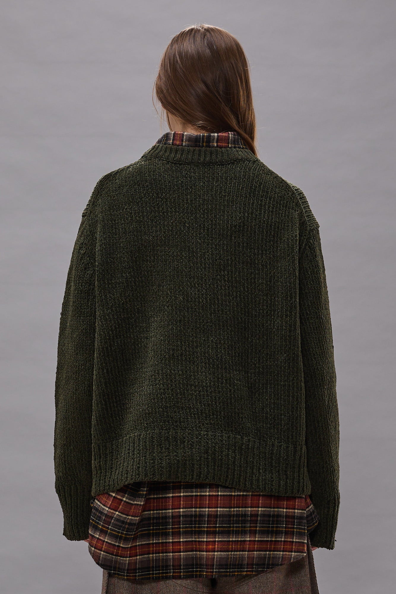 Olive green boxy crewneck sweater with ribbed texture, shown from back on model wearing plaid shirt underneath.