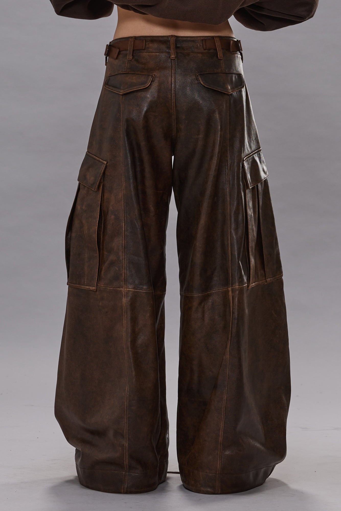 Brown leather cargo pants with side pockets, wide-leg silhouette, and stitched seams, shown from back view.